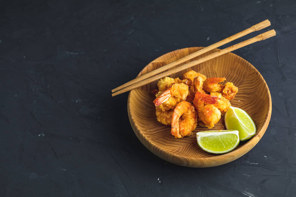 Fried Shrimps tempura with lime in wooden plate on dark concrete surface background. Copy space for you text. Seafood tempura dish served japanese or eastern Asia style with chopsticks. - Fotoğraf, Görsel