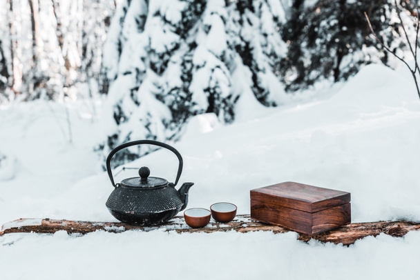 czajnik z małych filiżanek na powierzchni drewnianych w śnieżnym lesie - Zdjęcie, obraz
