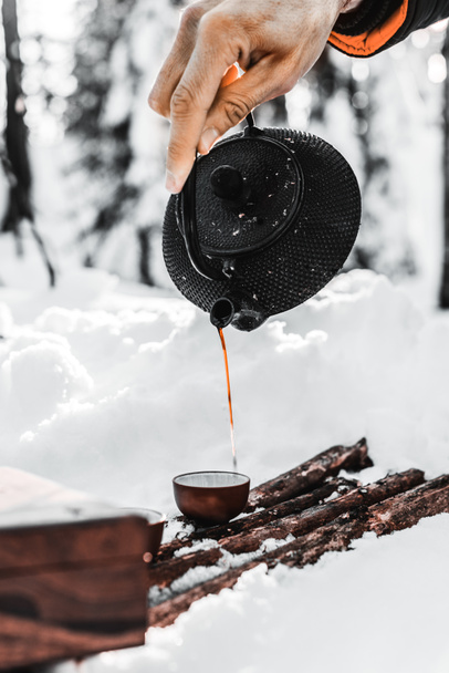 partial view of male traveler pouring tea from kettle in cup in winter forest - Fotoğraf, Görsel