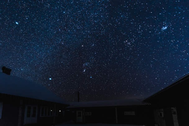 έναστρο ουρανό σκοτεινό και σπίτια καλυμμένα με χιόνι τη νύχτα το χειμώνα - Φωτογραφία, εικόνα