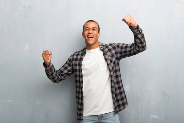 Young african american man with checkered shirt celebrating a victory in winner position - Foto, Imagen