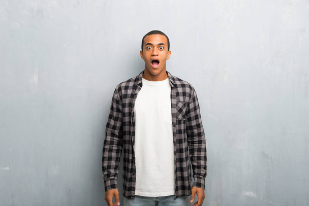 Joven hombre afroamericano con camisa a cuadros con sorpresa y expresión facial impactada
 - Foto, imagen