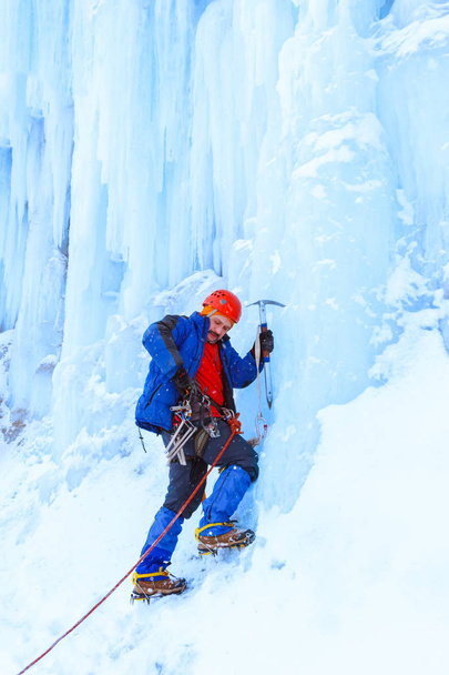 Bergsteiger mit Eispickel bereitet sich auf die Besteigung einer schneebedeckten Eiswand vor - Foto, Bild