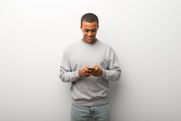 African american man on white wall background sending a message or email with the mobile - 写真・画像