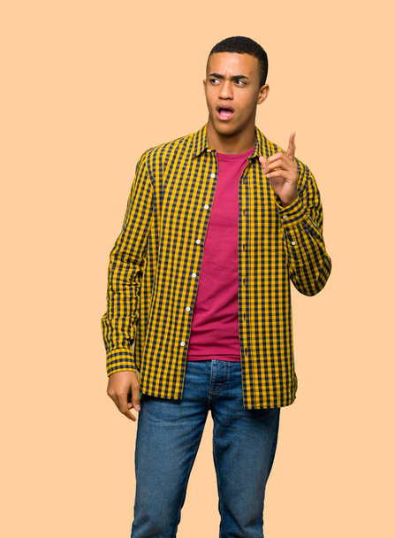 Young afro american man thinking an idea pointing the finger up on isolated background - 写真・画像