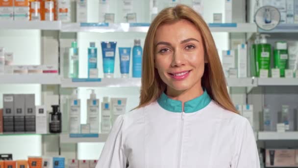 Beautiful female pharmacist smiling, holding blister of capsules at drugstore - Felvétel, videó
