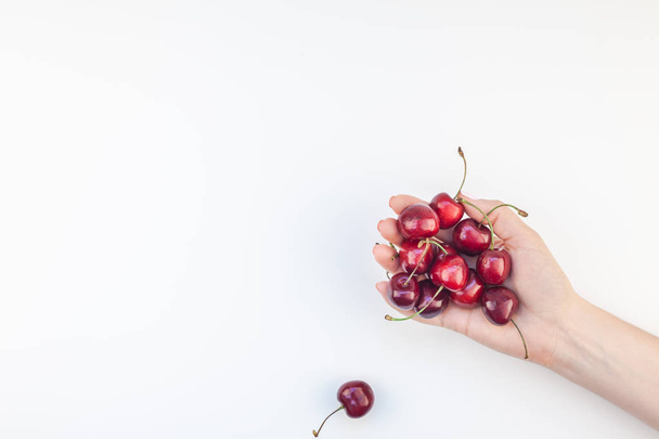 Creative top view of fresh ripe cherry in a female hands with copy space isolated on white background in minimal style. Concept of summer fun and healthy eating. Template for your text or food design - Photo, Image