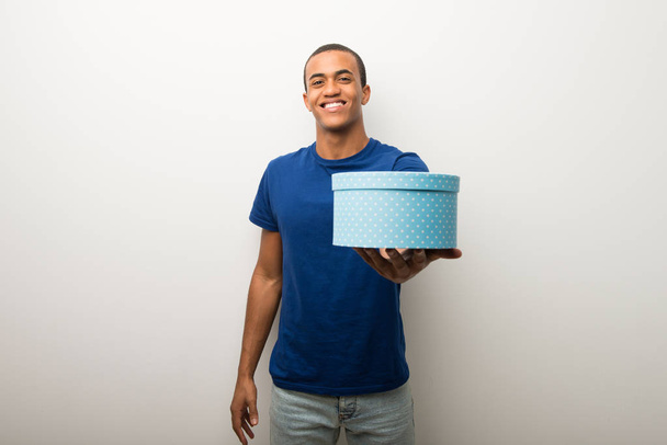 Afro-amerikai fiatalember fehér falon, kezében egy ajándék gazdaság - Fotó, kép