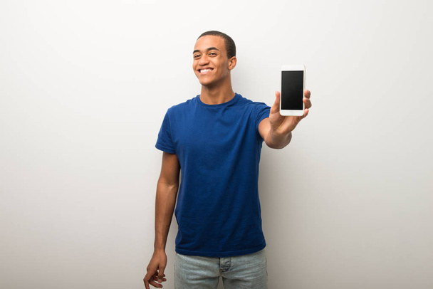 Jonge Afro-Amerikaanse man op de witte muur tonen de mobiele - Foto, afbeelding