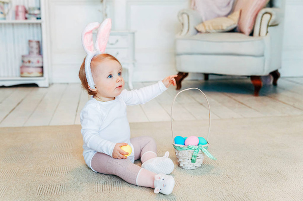 Μικρό παιδί κορίτσι φορώντας τα αυτιά λαγουδάκι ανήμερα του Πάσχα και παίζοντας με ζωγραφισμένα αυγά - Φωτογραφία, εικόνα