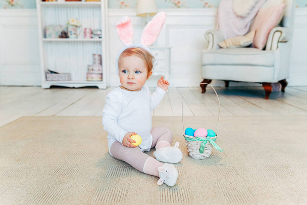 Malá holka dítě nosí uši zajíček velikonoční den a hrát si s malovanými vejci - Fotografie, Obrázek