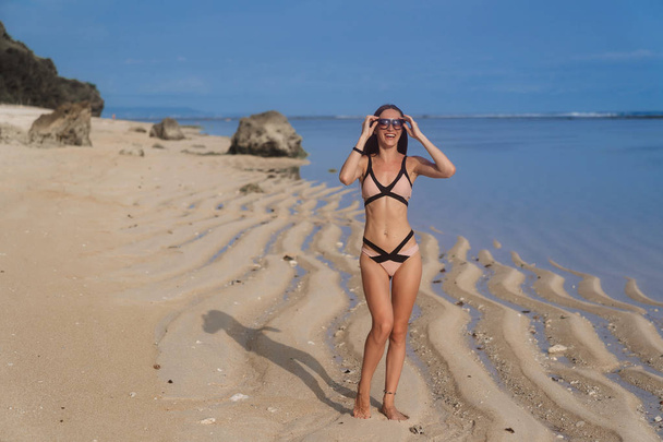 Sexy girl in swimsuit with sunglasses posing on sandy beach - Foto, Bild