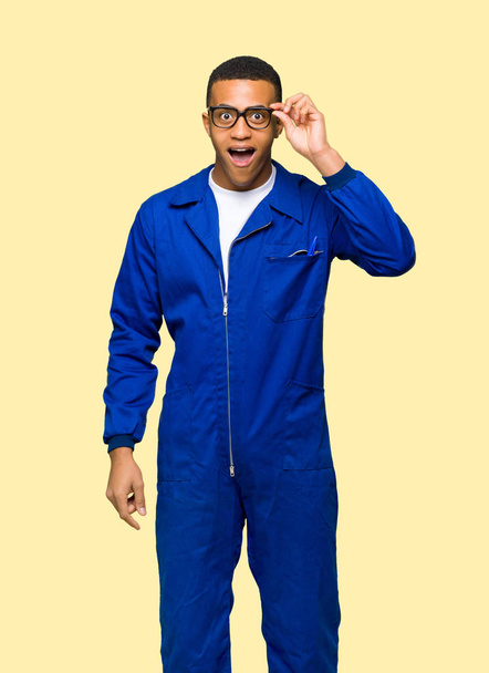Mladý afro americký dělník muž s brýlemi a překvapen na izolované pozadí - Fotografie, Obrázek