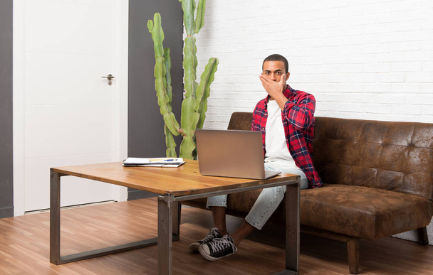 Afrikai amerikai férfi laptop borító száj, kezével, mondván valami alkalmatlan a nappaliban - Fotó, kép