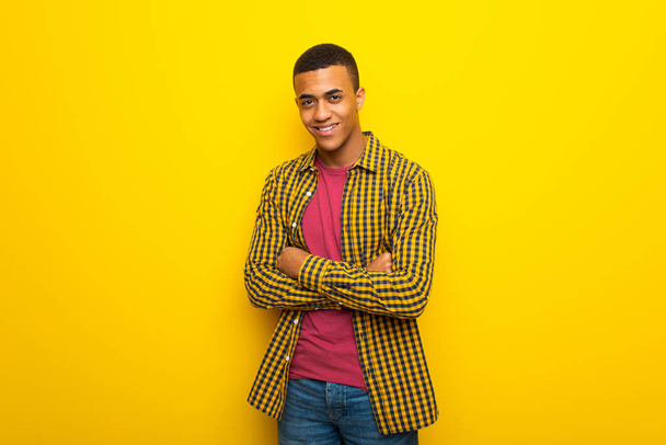junger afroamerikanischer Mann auf gelbem Hintergrund, der die Arme frontal verschränkt hält - Foto, Bild