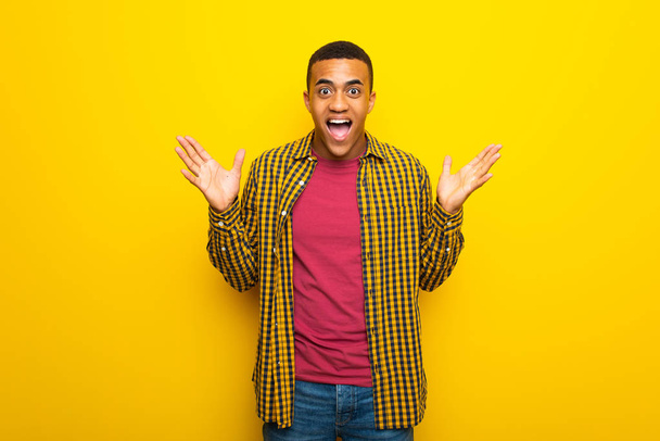 Joven afroamericano sobre fondo amarillo con expresión facial sorpresa y conmocionada
 - Foto, Imagen