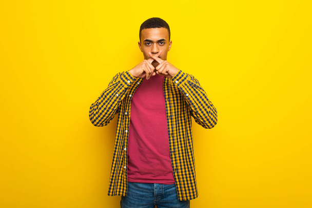 Nuori afroamerikkalainen mies keltaisella pohjalla osoittaa hiljaisuuden elettä
 - Valokuva, kuva