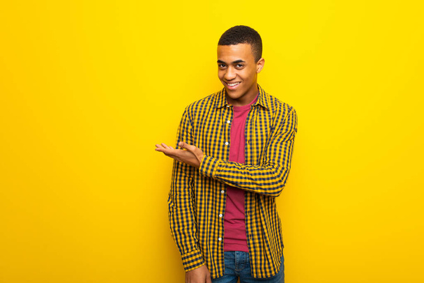 Afro Αμερικανός νεαρός σε κίτρινο φόντο, παρουσιάζοντας μια ιδέα ενώ αναζητούν χαμογελώντας προς - Φωτογραφία, εικόνα