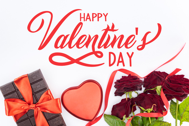 vue du dessus du chocolat enveloppé d'un ruban festif, de roses rouges et d'une boîte cadeau en forme de coeur isolée le jour de la Saint-Valentin blanche et heureuse
   - Photo, image