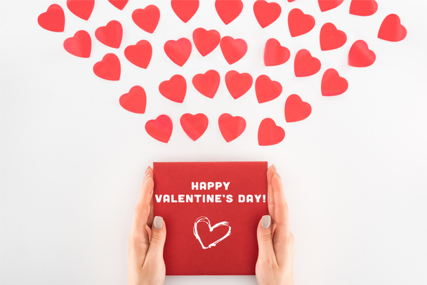 cropped shot of woman holding envelope with "Happy valentines day" lettering under dozen red heart symbols isolated on white  - Photo, Image