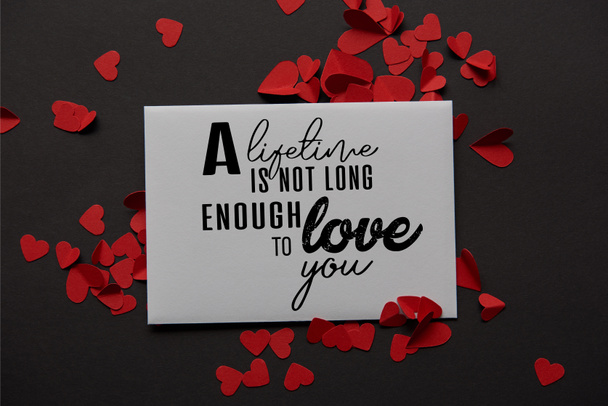 top view of greeting card with "a lifetime is not long enough to love you" lettering and red paper cut hearts on black background  - 写真・画像