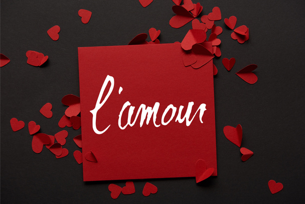 top view of red greeting card with "lamour" lettering and paper cut hearts on black background - Photo, Image