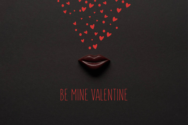 top view of tasty chocolate lips on black background with "be mine valentine" lettering  - Fotografie, Obrázek