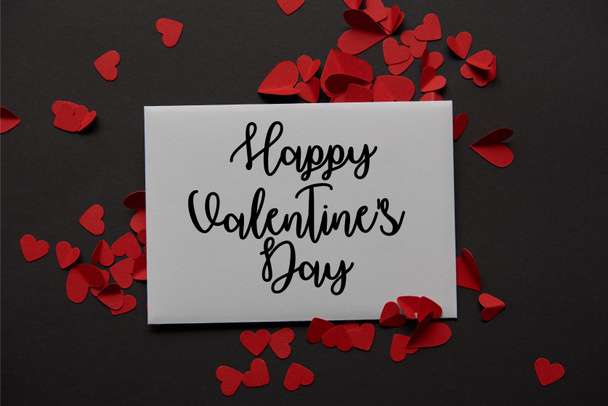 вид зверху вітальної листівки з написом "З днем Святого Валентина" та червоним папером вирізані серця на чорному тлі
 - Фото, зображення