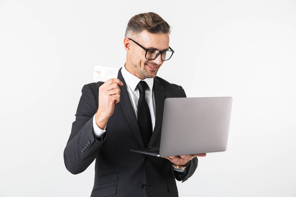 Imagen de un hombre de negocios guapo aislado sobre fondo blanco de la pared usando computadora portátil con tarjeta de crédito
. - Foto, Imagen