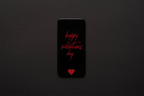 vista superior del teléfono inteligente con letras de "Feliz día de San Valentín" y un pequeño letrero rojo del corazón sobre fondo oscuro
 - Foto, imagen