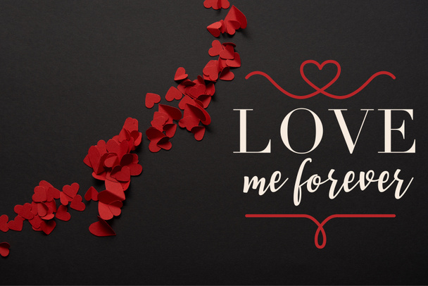 top view of red small paper cut hearts on black background with "love me forever" lettering - Zdjęcie, obraz