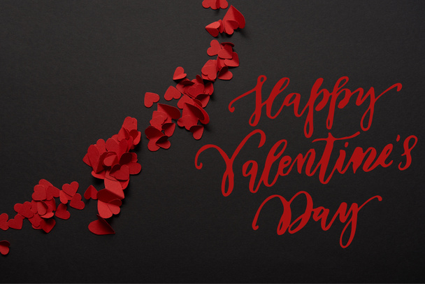 vista superior do vermelho pequeno papel cortar corações no fundo preto com "Feliz Dia dos Namorados" lettering
 - Foto, Imagem