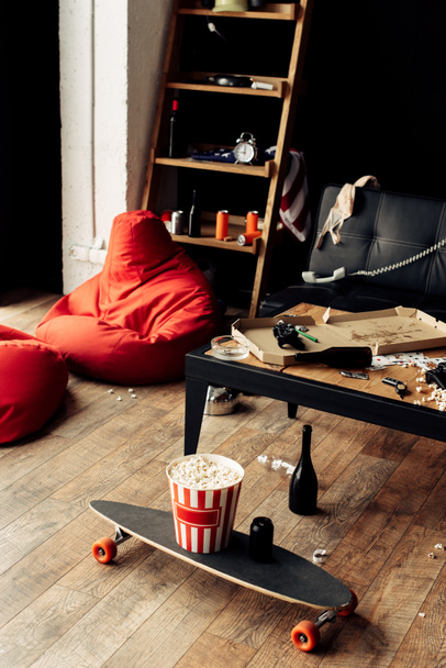 skateboard met popcorn vak in de buurt van koffietafel in rommelige woonkamer - Foto, afbeelding