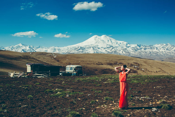 brunette woman in long red dress on the background of high snow-capped mountains  - Foto, afbeelding
