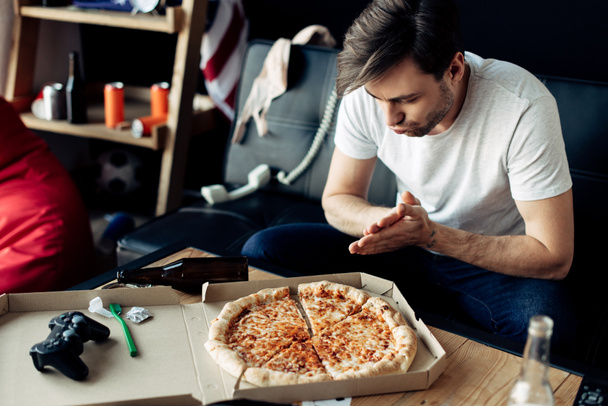 man looking at tasty pizza in messy living room after party - Foto, Imagen