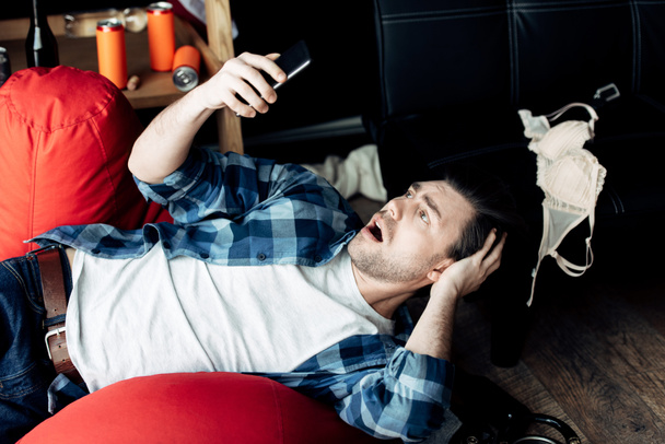 překvapený muž ležící na blůzku a při pohledu na smartphone - Fotografie, Obrázek