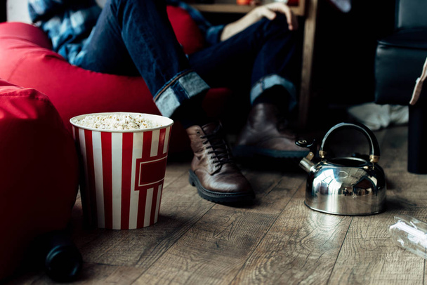 rajattu näkymä mies istuu papu pussi lähellä popcorn laatikko kotona
  - Valokuva, kuva