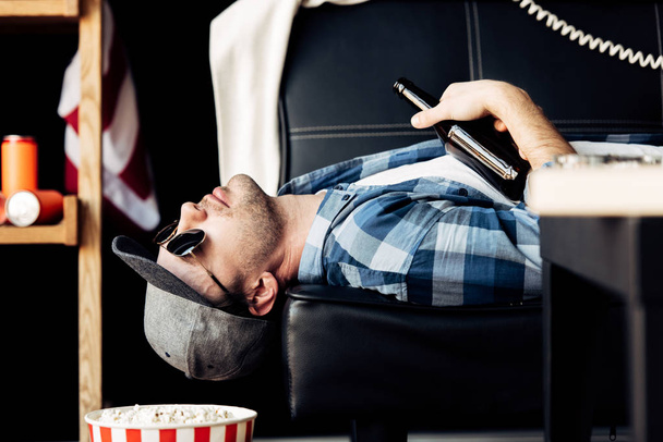 όμορφος άντρας ξαπλωμένος στον καναπέ και κρατώντας το μπουκάλι μετά το κόμμα - Φωτογραφία, εικόνα