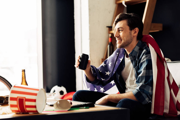 χαρούμενος άνθρωπος που κρατά μπορεί με μπύρα και συνεδρίαση με την αμερικανική σημαία  - Φωτογραφία, εικόνα
