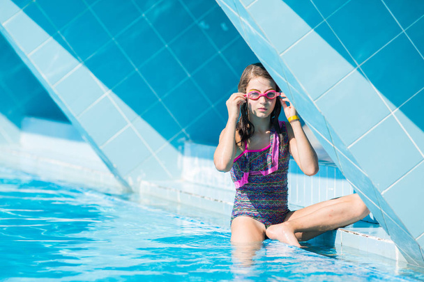 κορίτσι σε ένα μαγιό που κάθεται στο πλάι στην πισίνα και φοράει γυαλιά κολύμβησης - Φωτογραφία, εικόνα