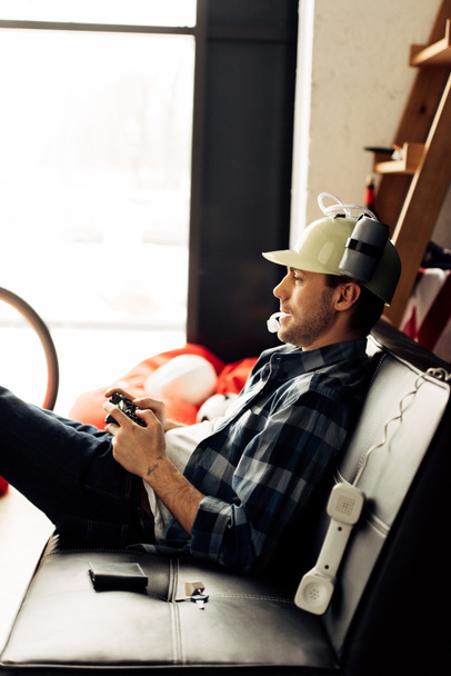 cheerful man drinking from beer helmet and playing video game at home - Photo, Image