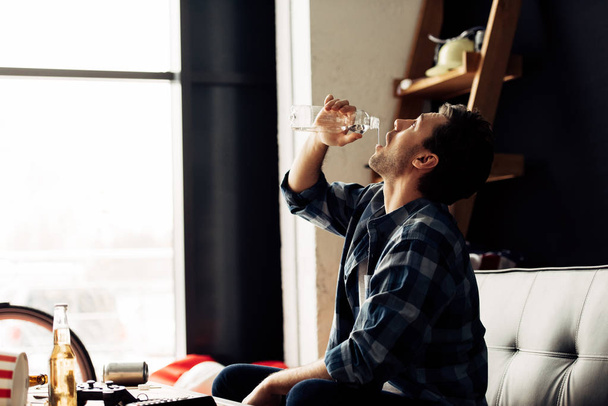 homem bonito bebendo água enquanto sentado no sofá
 - Foto, Imagem