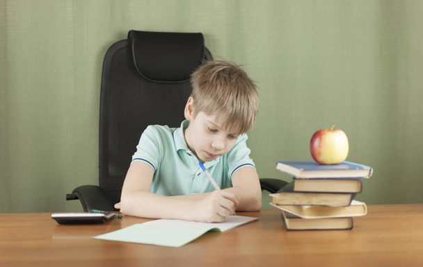 Smart school chłopiec siedzi przy stole z wielu książek i czerwone jabłko. Koncepcja kształcenia.  - Zdjęcie, obraz
