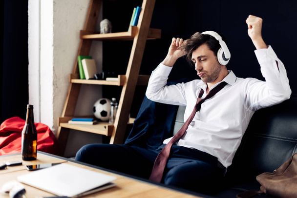 pohledný muž poslech hudby ve sluchátkách poblíž konferenční stolek  - Fotografie, Obrázek