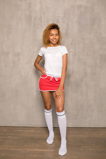 Young African American woman in a white T-shirt and a bright sports skirt. - Фото, зображення