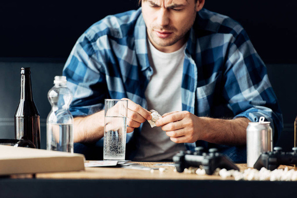 man suffering from hangover holding aspirin and looking at glass of water - Foto, afbeelding