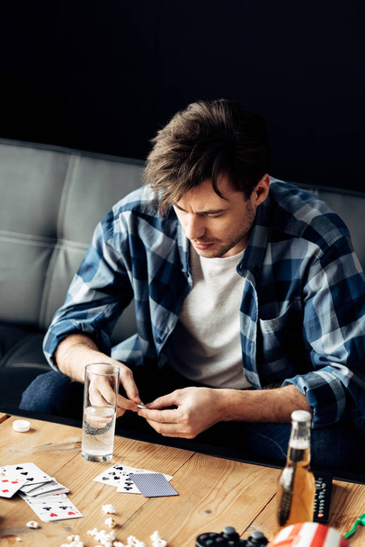 man looking at aspirin near glass of water in messy living room - Foto, afbeelding
