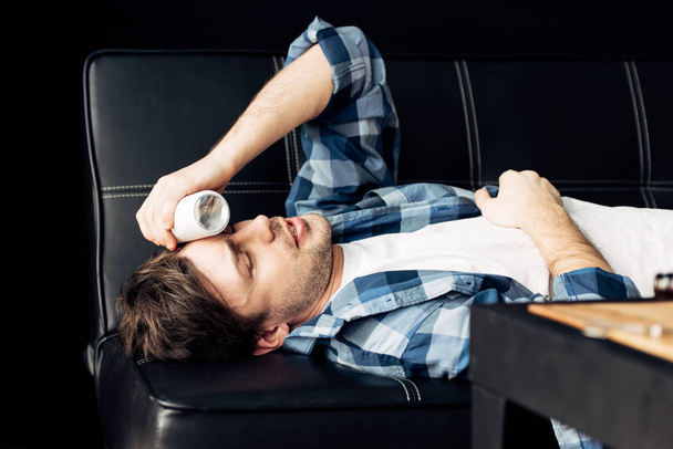 man lying on sofa and holding bottle near head after party - Foto, immagini