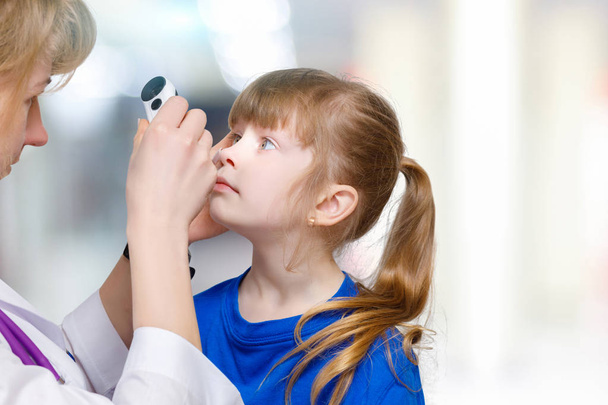 A closeup of female ophthalmologist examining eyes of small child with special equipment at hospital room background. The concept of eye problems treatment. - Photo, Image