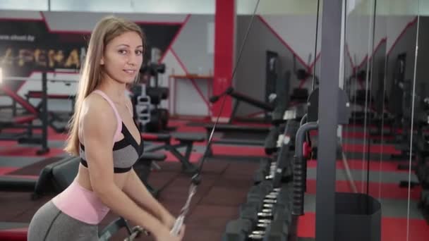 La chica realiza la extensión de los brazos para el tríceps en un simulador de bloque
 - Imágenes, Vídeo